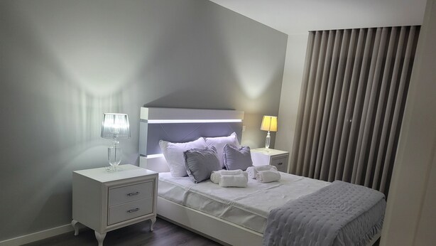 Un dormitorio de hotel moderno con una cama, dos mesitas de noche, una lámpara y una ventana con cortinas.