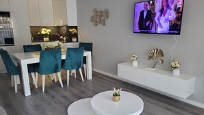 Una sala de estar moderna con comedor, un televisor montado en la pared y una consola blanca con objetos decorativos.