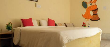 A hotel room with a large bed, a nightstand, a small table with a plant, and a wall mural.
