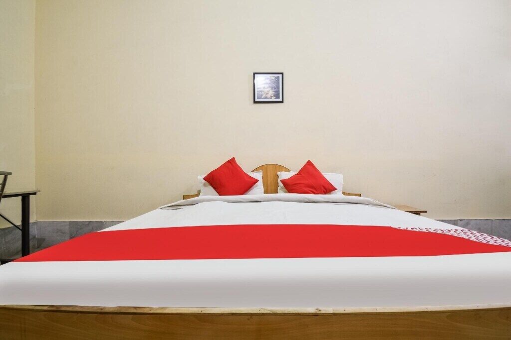 A single bed with a red and white bedspread, two red pillows, and a wooden headboard.