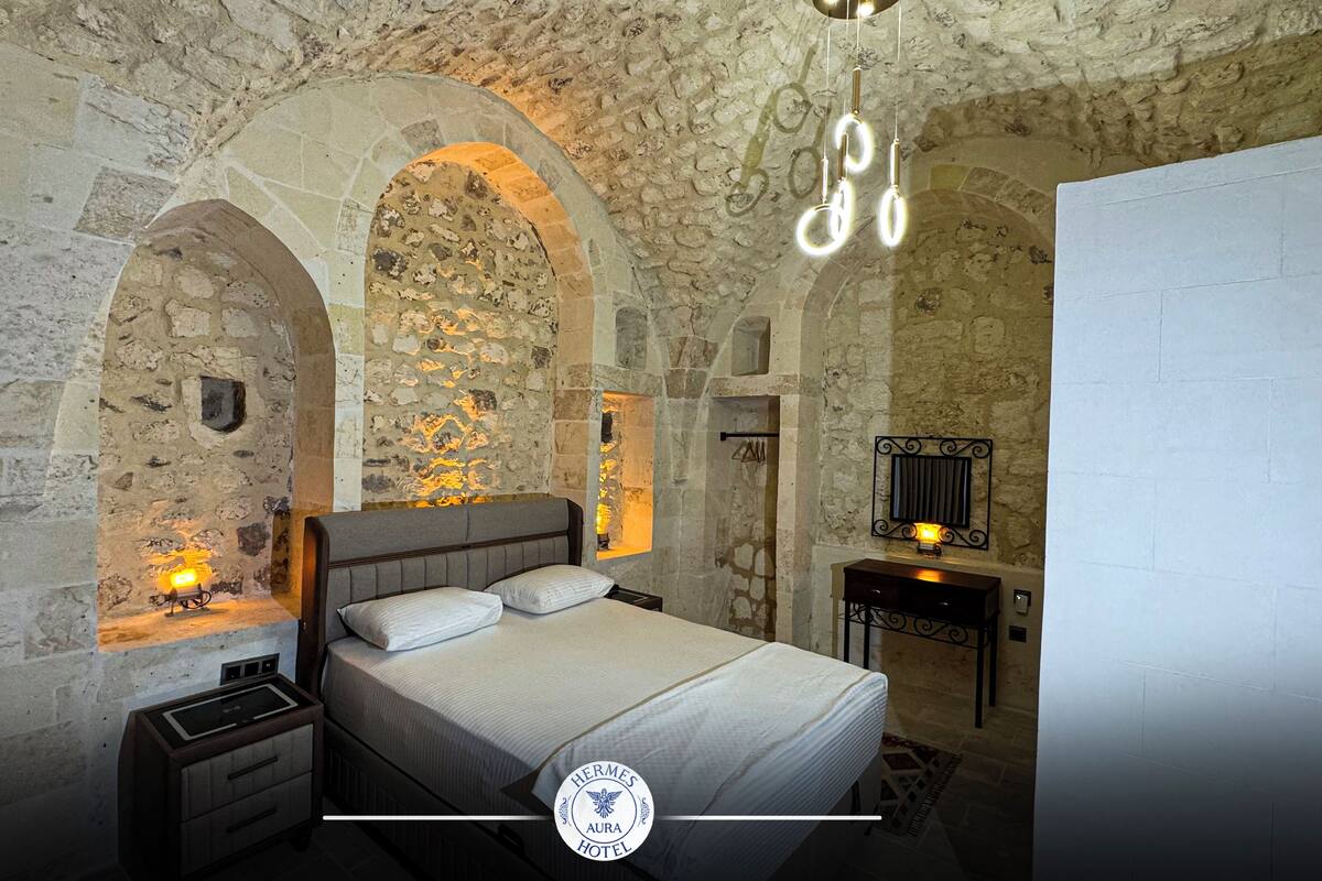 A bedroom with a stone wall, a bed with a headboard, a nightstand, and a wall-mounted light fixture.