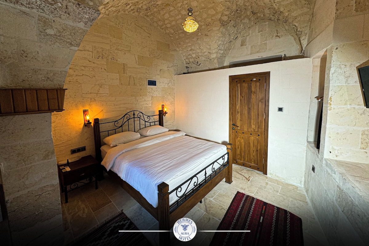 A bedroom with a stone wall, a wooden door, a bed with white bedding, and two wall-mounted lights.