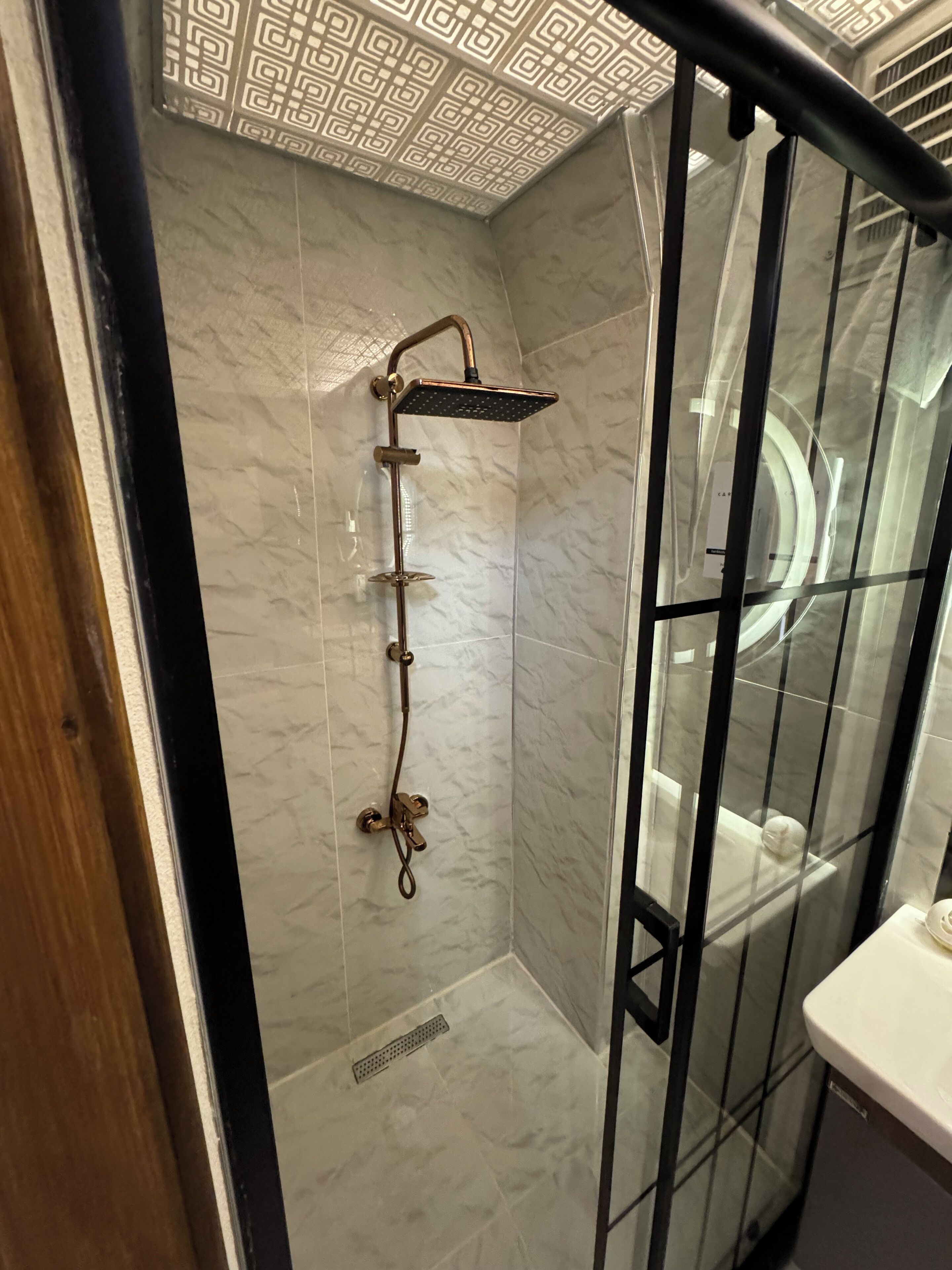 A bathroom with a glass-enclosed shower, marble walls, and a wooden door frame.