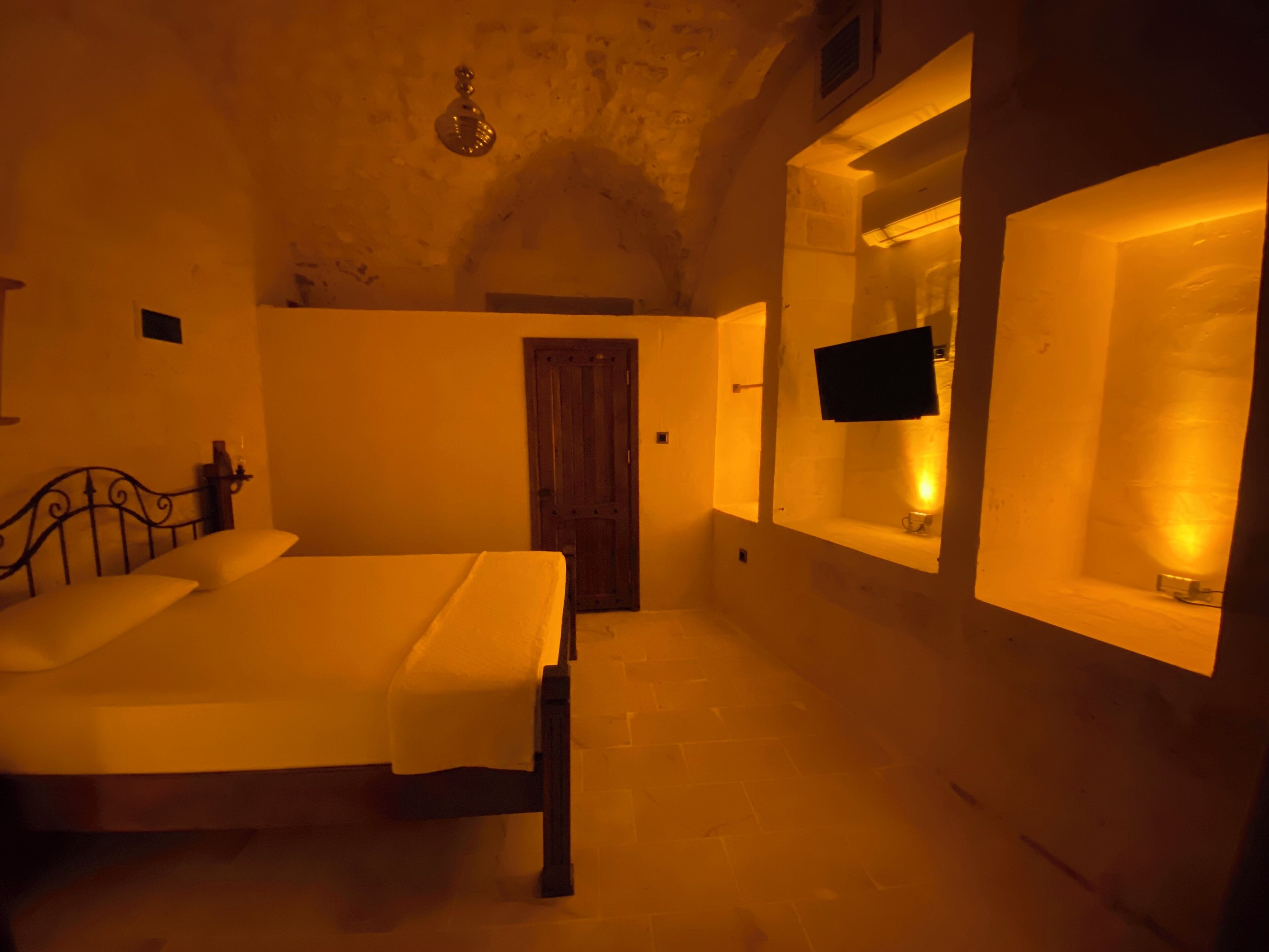 Un dormitorio con una cama, una puerta de madera, un espejo y un televisor montado en la pared.