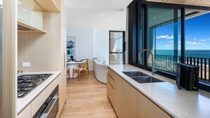 Une cuisine moderne dotée d’une grande fenêtre donnant sur l’océan, d’un plancher en bois et d’un coin repas avec une chaise et une table.