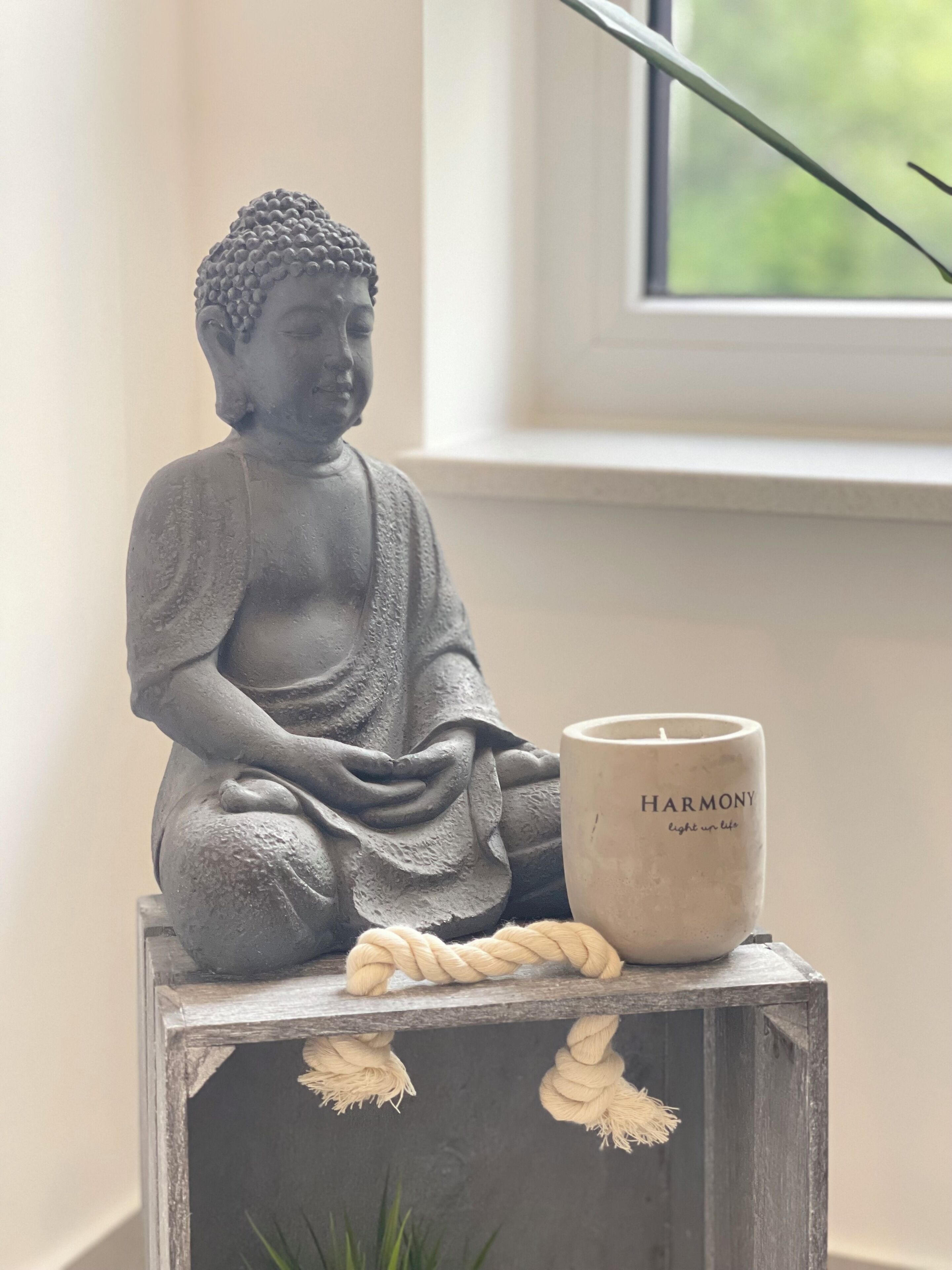 Une statue représentant une figure assise, peut-être un Bouddha, posée sur un bloc de bois, avec une bougie étiquetée « HARMONIE » à côté.