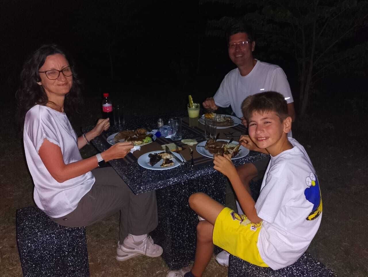 Um grupo de pessoas jantando em uma mesa ao ar livre com toalha de mesa azul.