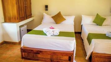 Habitación de hotel con dos camas, cada una con ropa de cama blanca y almohadones verdes. Hay un banco de madera al pie de las camas, y un pequeño escritorio con una lámpara.