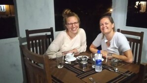 Two people seated at a wooden dining table with chairs, a water bottle, and a glass on the table. - Tiara Elephant Lodge (Habarana)