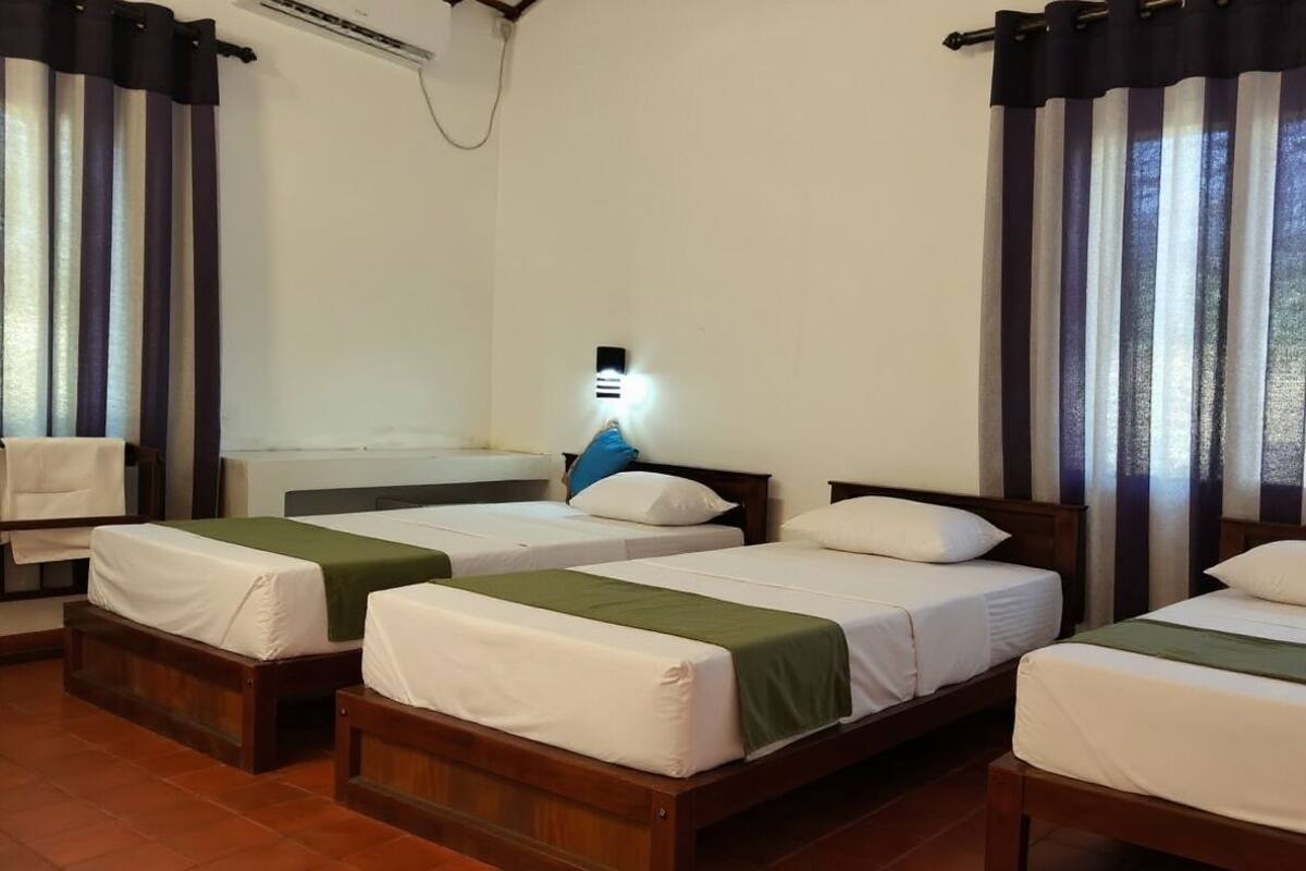 A hotel room with four single beds, a small table, and a nightstand.
