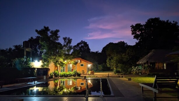 A nighttime view of a resort with a swimming pool, a small building with lights, and surrounding trees. - Tiara Elephant Lodge (Habarana)