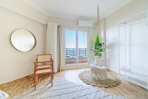 Una habitación con una silla de madera, una hamaca colgante, un espejo redondo y vista al mar a través de una puerta corredera.