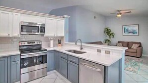 A modern kitchen with a built-in oven, microwave, and dishwasher, a sink, and a dining area with a couch.