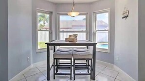 A dining area with a table and bench, large windows, and a hanging light fixture.