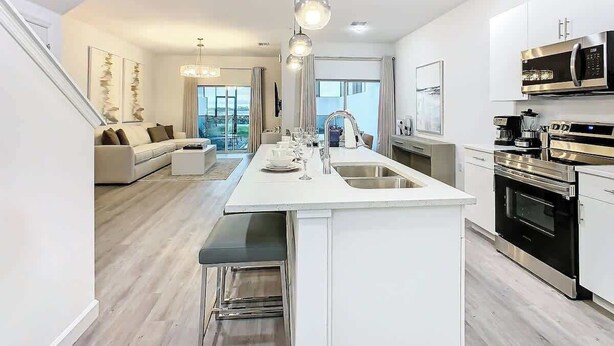 A modern kitchen with a central island, stainless steel appliances, and a view to the living area. - 6BR Home w/ Private Pool, 15min to Disney + More! (Davenport)