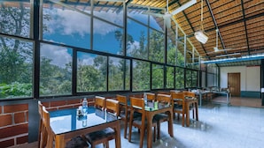 Uma sala de jantar espaçosa com amplas janelas, mesas e cadeiras de madeira.