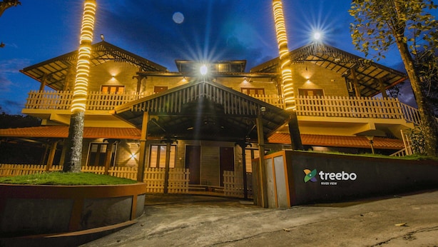 Um hotel com entrada coberta, cerca branca de piquete e uma placa com a inscrição 'treebo River View'.
