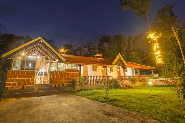 A two-story building with a brick facade and a tiled roof. There is a visible entrance with steps leading up to it. - Treebo River View (Madikeri)