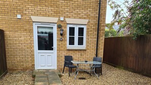 A brick house with a white door, a small patio with a table and chairs, and a gravel path leading to the door. - 3 Bed, Cozy and Comfortable Retreat (Spalding)