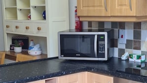 A kitchen with wooden cabinets, a microwave, and a small oven. - 3 Bed, Cozy and Comfortable Retreat (Spalding)