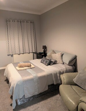 A bedroom with a bed, a nightstand, a lamp, and a chair.
