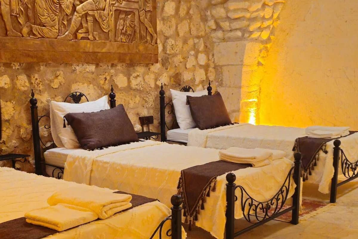 A hotel room with three beds, each with a different style of headboard and pillows. The room has stone walls and a large mural above the beds.