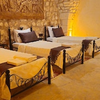 Habitación de hotel con tres camas, cada una con un estilo diferente de cabecera y almohadas. La habitación tiene paredes de piedra y un gran mural sobre las camas.