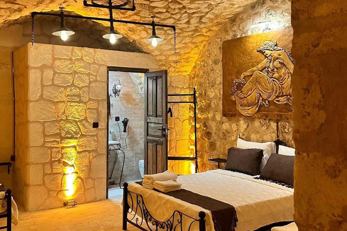 A stone-walled bedroom with a bed, a hanging light fixture, and a painting on the wall.