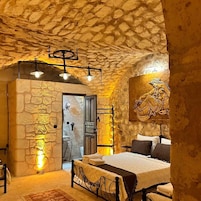 Un dormitorio de paredes de piedra con una cama, un lámpara colgante y un cuadro en la pared.