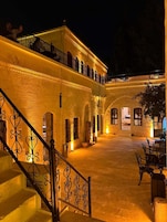 Un patio con una escalera que lleva a un balcón, rodeado de muros y arcos de piedra.