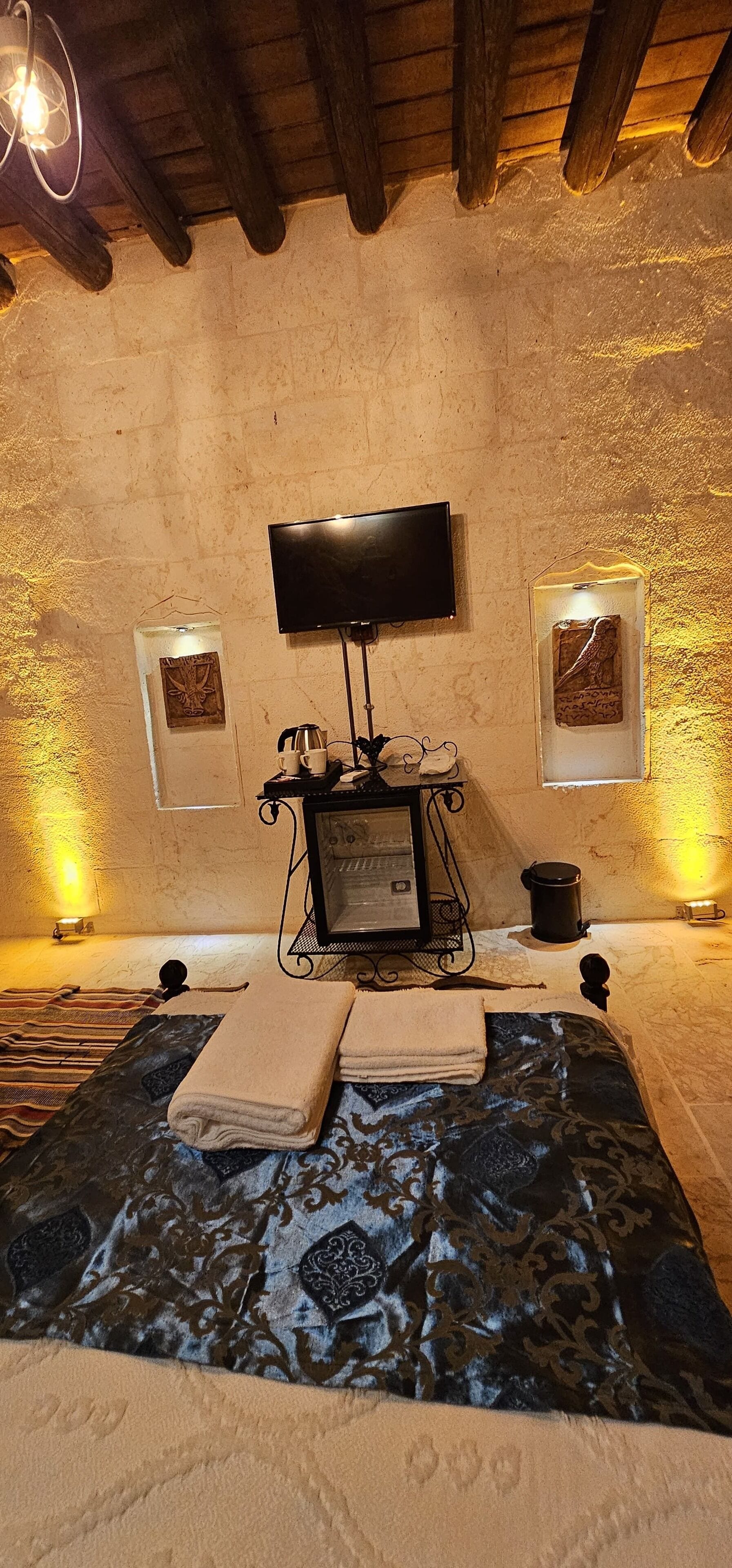 A cozy room with a bed, a flat-screen TV mounted on the wall, and two framed artworks on the walls.