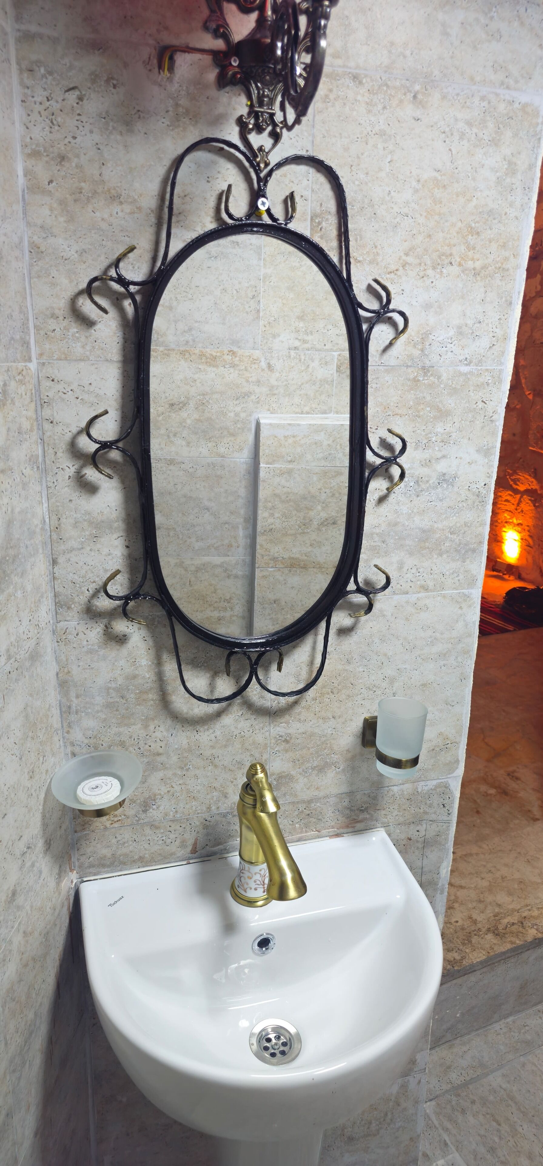 A bathroom with a white sink, a gold faucet, and a black ornate mirror.