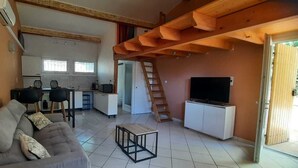 Un saló amb un sofà, una televisió, una zona de cuina i una escala.
