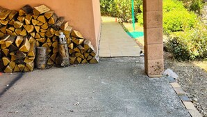 Zona exterior coberta amb llenya apilada i un llum d'aquesta, que condueix a un camí i vegetació.