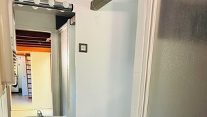 Un bany amb un lavabo blanc, un mirall i un vàter. Hi ha un safata de brossa i una porta que dona a una altra habitació.