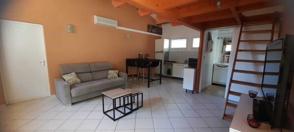 Un salon comprenant un canapé, une table basse et un coin cuisine avec un réfrigérateur, une cuisinière et un évier.
