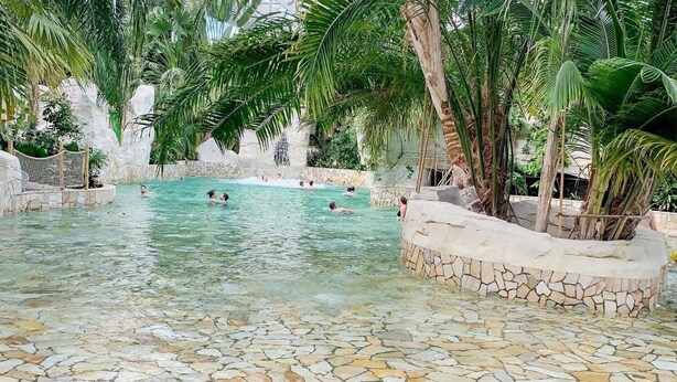 Una piscina interior con agua cristalina, rodeada de muros de piedra y palmeras.