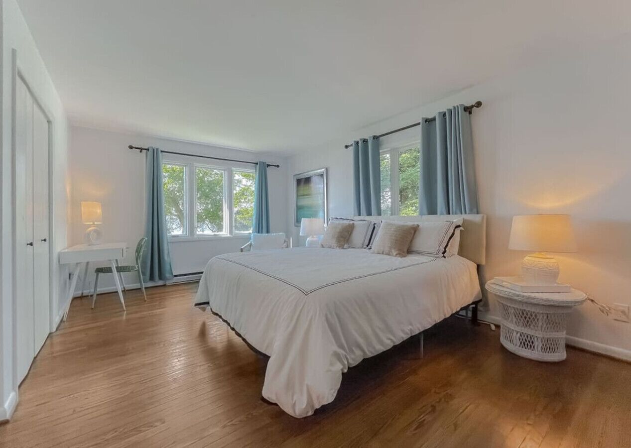 A bedroom with a large bed, a bedside table, a chair, a desk, and a window with curtains.