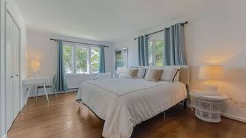 A bedroom with a large bed, a bedside table, a chair, a desk, and a window with curtains.
