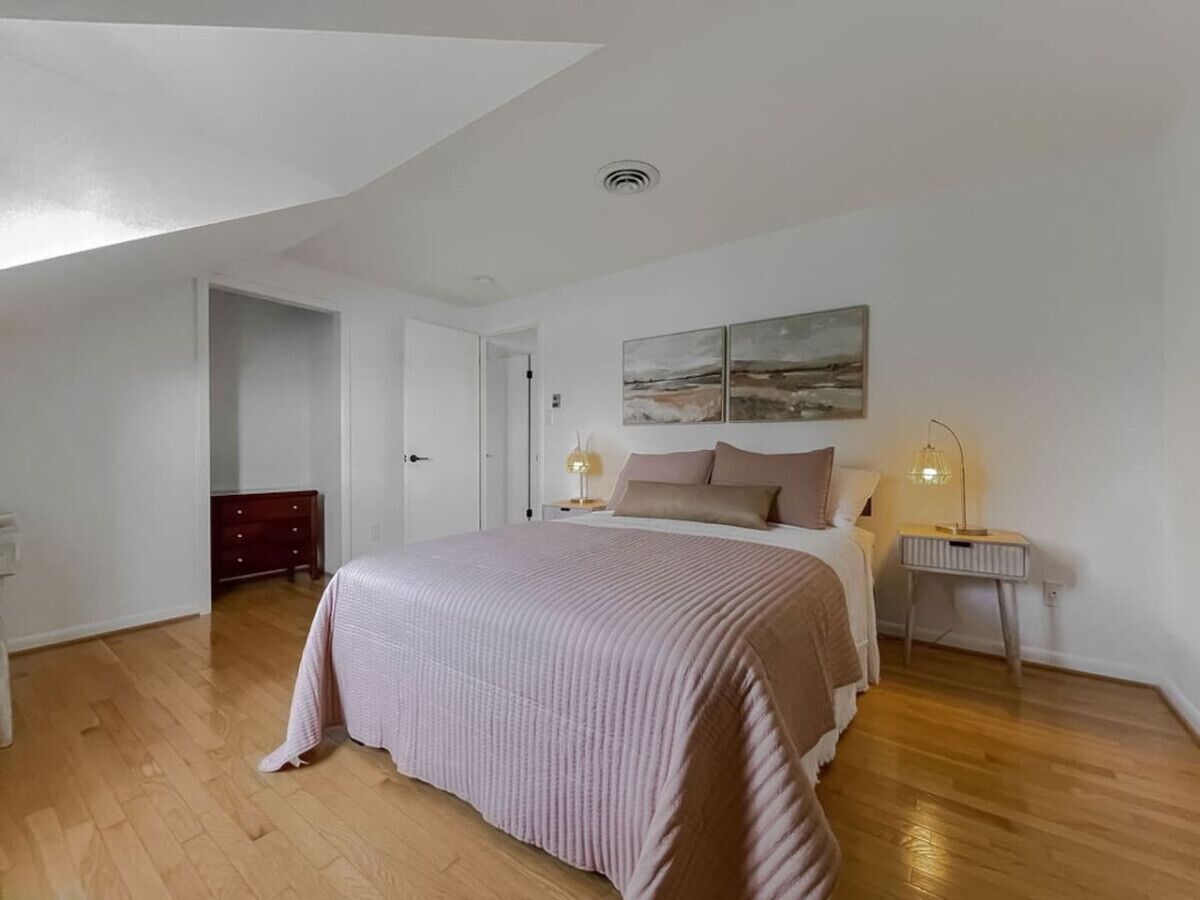 A bedroom with a large bed, a bedside table with a lamp, a door leading to another room, and a painting on the wall.