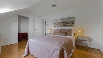 A bedroom with a large bed, a bedside table with a lamp, a door leading to another room, and a painting on the wall.