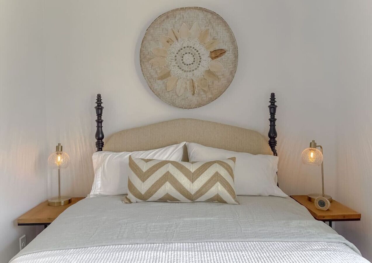 A neatly made bed with a patterned pillow, a decorative wall hanging, and two bedside lamps on wooden nightstands.