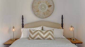 A neatly made bed with a patterned pillow, a decorative wall hanging, and two bedside lamps on wooden nightstands.