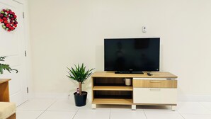 En moderne stue med et fladskærms-tv på et træ-tv-bord, en lille potteplante og en hvid dør med en rød krans.