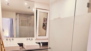 Un baño moderno con dos lavamanos, cabina de ducha de cristal y un espejo grande.