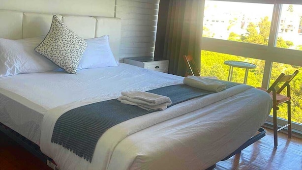 Habitación de hotel con una cama grande, una mesita pequeña y vistas a zonas verdes por la ventana.