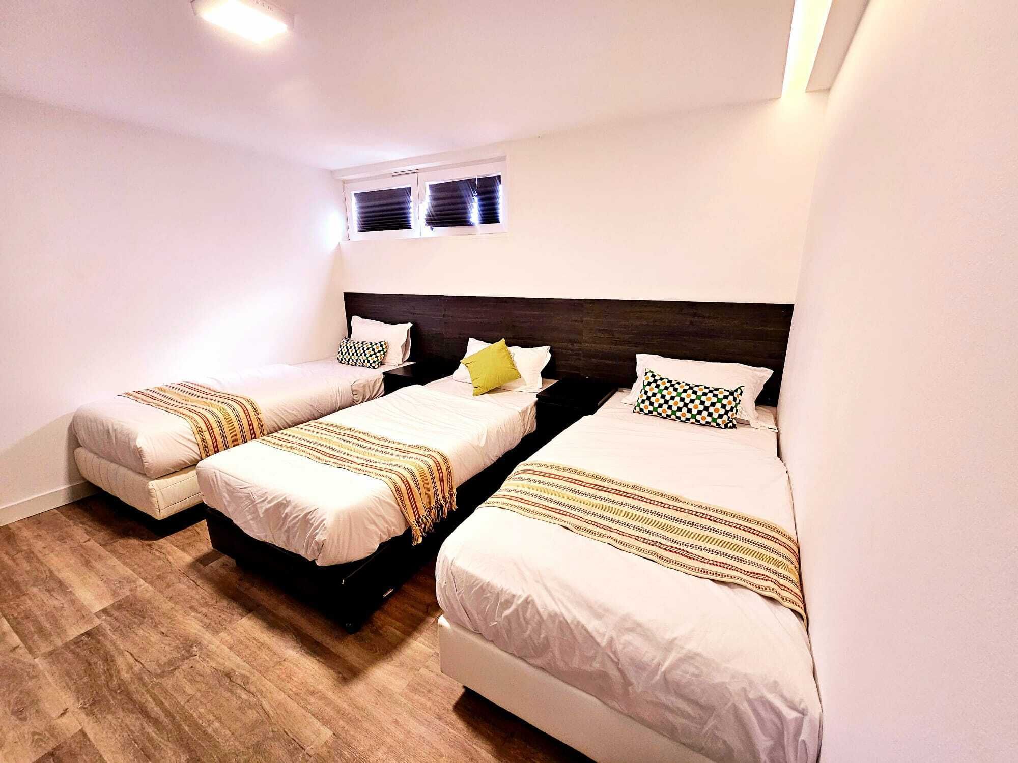 Una habitación de hotel con tres camas individuales, piso de madera y una ventana con persianas.
