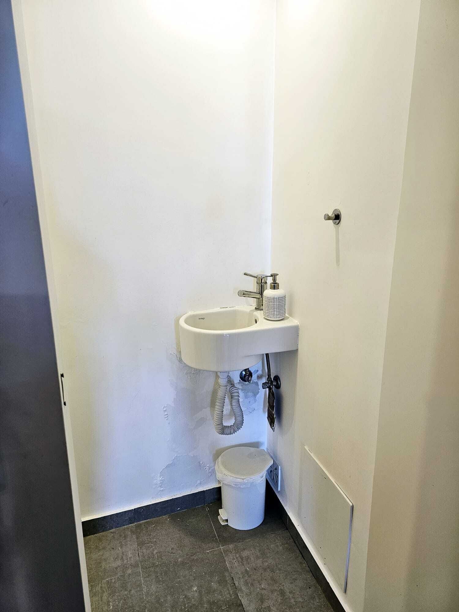 A small bathroom with a white sink, a toilet, and a white bucket.