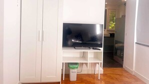 Una habitación con un armario blanco, un televisor de pantalla plana sobre un soporte blanco y un cubo de basura pequeño.
