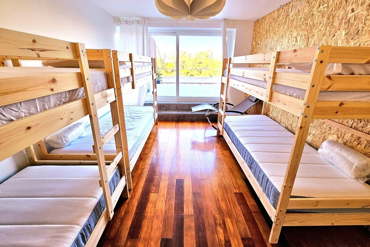 Un dormitorio con literas, suelo de madera y un ventanal con vistas a zonas verdes.